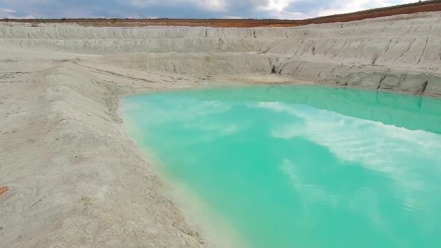 Close aerial view of bright turquoise water contrasting with white kaolin clay formations in an abandoned open pit quarry.