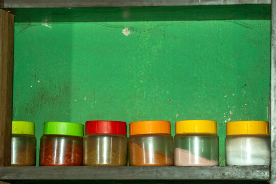 Row of six colorful plastic spice jars on dark wooden kitchen shelf.