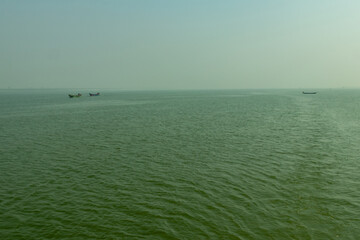 Small fishing boats drifting on vast green sea under misty sky view. © mssozib