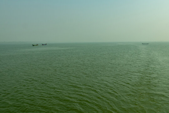 Small fishing boats drifting on vast green sea under misty sky view.