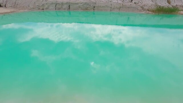 Detailed view of turquoise mineral-rich water surrounded by pale kaolin clay deposits in an abandoned quarry.