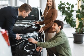 Smiling Caucasian Couple Engaging With Male Salesperson Discussing Features Of A Black Suv At Auto...