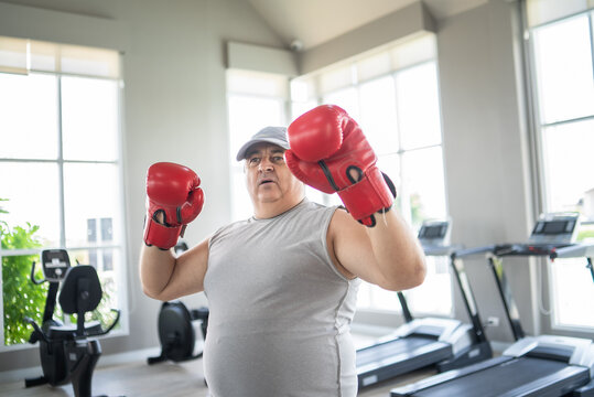 An overweight mature man wearing boxing gloves and sportswear in a bright fitness center indoor gym, focusing on strength, health, active lifestyle, and personal wellness training.