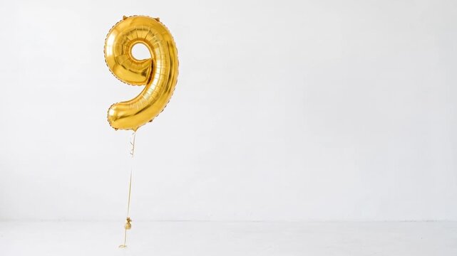 Large gold number nine helium balloon floating against a clean white background with copy space, ideal for ninth birthday, anniversary, milestone and celebration concepts.