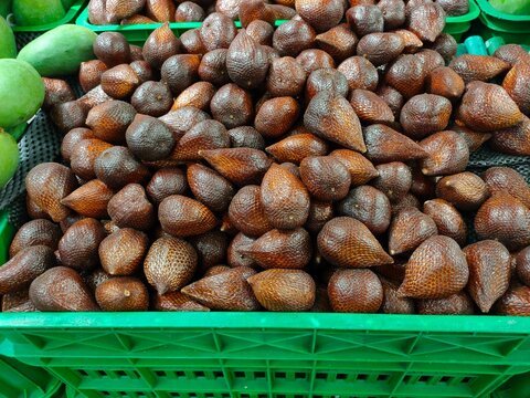 A green crate overflowing with brown, scaly snake fruit (salak pondoh) in a store display.