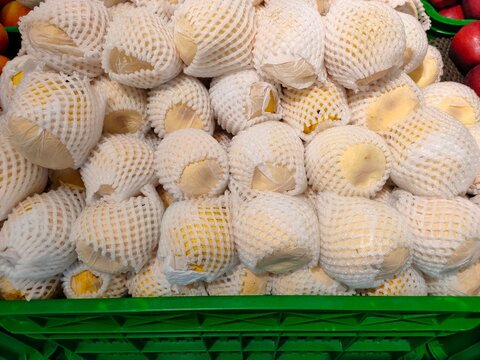 A green crate filled with fresh pears individually wrapped in white protective foam mesh sleeves at a grocery display.