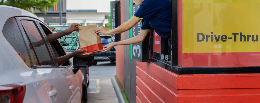 Hand Man in car receiving coffee in drive thru fast food restaurant. Staff serving takeaway order for driver in delivery window. Drive through and takeaway for buy fast food for protect covid19.