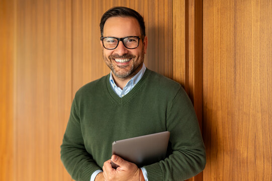 Professional man holding a digital tablet, smiling confidently at the camera, embodying expertise and successful business management in a corporate environment