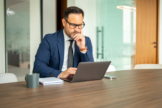 Professional businessman concentrating on legal documents, working on laptop, developing strategies, reviewing reports, making important decisions in a modern office