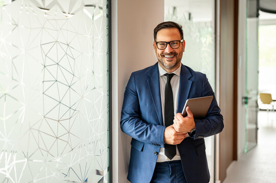 Business executive standing in modern corporate environment, holding digital tablet and smiling, representing successful professional, financial consulting, and legal services