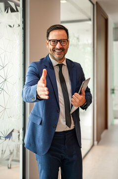 Smiling professional offering an open hand for a handshake in an office setting, conveying welcome, trust, partnership and friendly, confident business connection