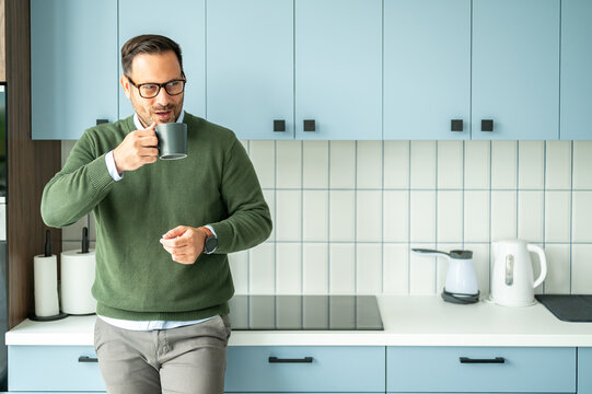 Businessman in glasses and a green sweater holding a mug, contemplating while taking a coffee break in a contemporary kitchen setting