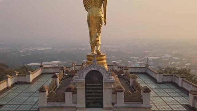 A big standing buddha statue at Wat Prathat Khao Noi and Nan province cityscape in background at dawn, Thailand