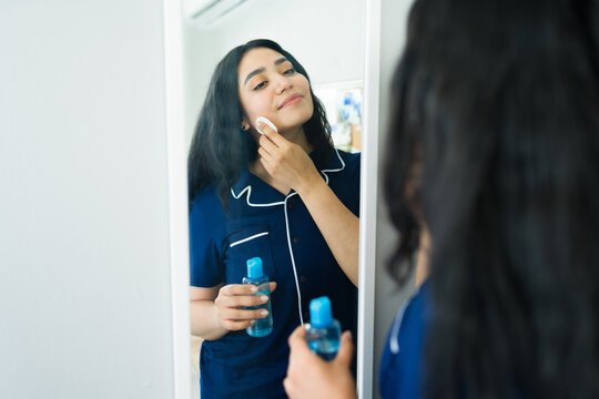 Latin woman applying facial toner to her skin with a cotton pad, following her daily skincare routine at home
