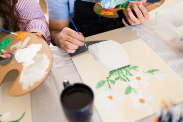 Closeup of students enjoying an art class, painting flowers on canvas, learning new skills and expressing creativity © AntonioDiaz