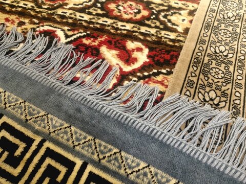 A close-up photograph showcasing the intricate decorative fringe and woven borders of traditional Persian and oriental carpets layered together.