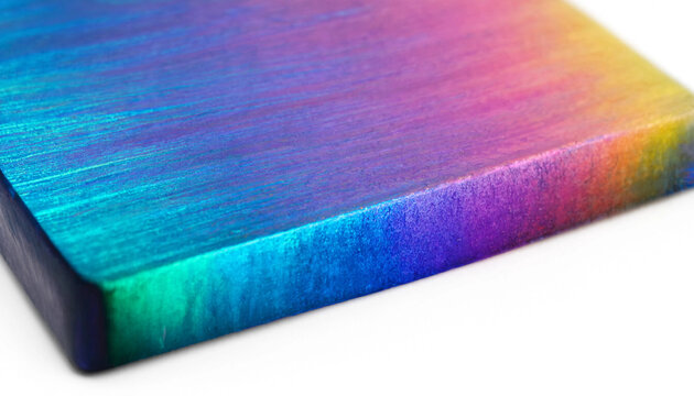Close up angle of anodized titanium metal plate displaying vibrant rainbow oxide heat gradient colors cyan purple orange isolated on white