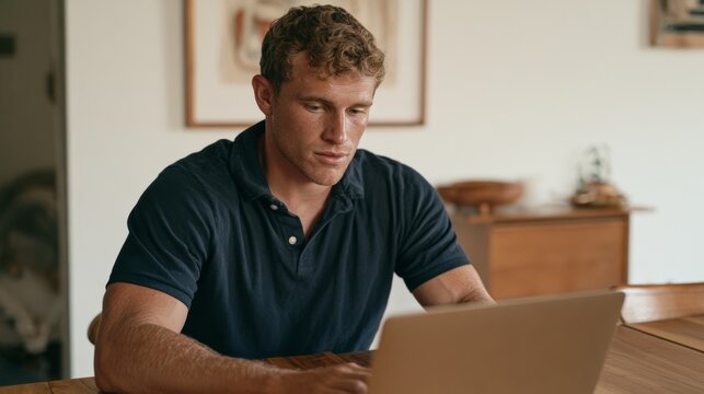 Man in Polo Shirt Sitting at Table with Laptop