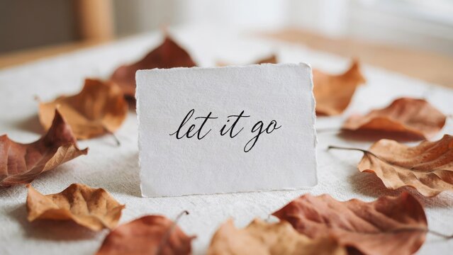 A handwritten message saying let it go on paper surrounded by dry autumn leaves. This inspirational concept can be used for mental health and mindfulness campaigns.