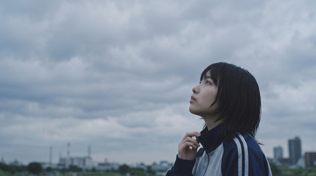 曇り空を見上げるアンニュイな表情の学生と進路や将来への不安
