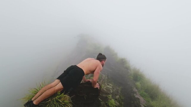 Man performing a push-up on a rocky mountain ridge, demonstrating strength and determination during a morning workout in the foggy, challenging environment of mount Batur, Bali