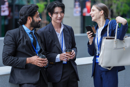 An Asian businessman, an Indian businessman and a European businesswoman look genuinely delighted during a team break in front of luxury retail frontage in a central business district
