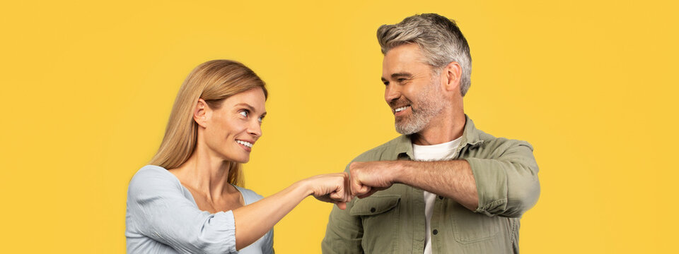 Smiling Caucasian Man And Woman Fist Bumping Together, Displaying Happy Emotion At A Studio Setting On Yellow Background. Positive Interaction Represents Business Collaboration And Teamwork Concept.