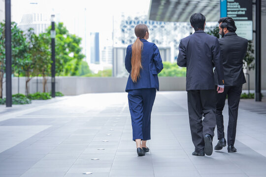 Three young business professionals wearing conference badges return to the office after a successful handshake in front of luxury retail frontage in a central business district