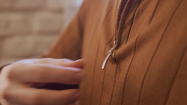 Close up of man buttoning zipper on his brown corduroy shirt with soft lighting and warm tones. hand wearing black ring moves steadily to fasten each zipper pull against fabric texture