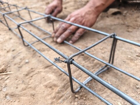 hand with Close-up view of a steel reinforcement bar framework arranged on the ground at a construction site, showing interconnected metal bars prepared for concrete foundation or structural work.