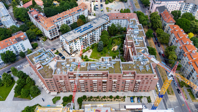 View of city buildings and construction site from above in a lively urban area. Aerial view of city buildings with construction ongoing on one side. Green spaces are visible.