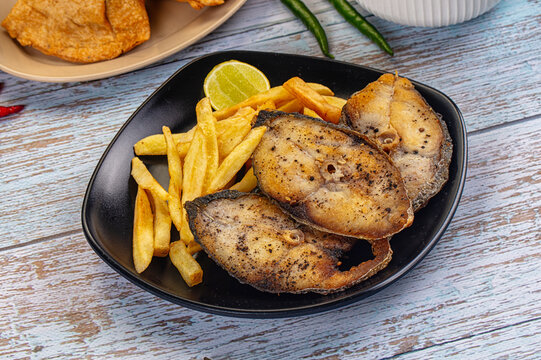 Grilled kingfish steaks with golden french fries and lime wedge on black plate over rustic blue wood table