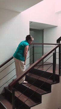 60s old senior asian woman slowly climbing staircase with knee joint pain or leg muscle atrophy, indoor home scene during daytime, health and body care and elderly mobility concept, vertical video