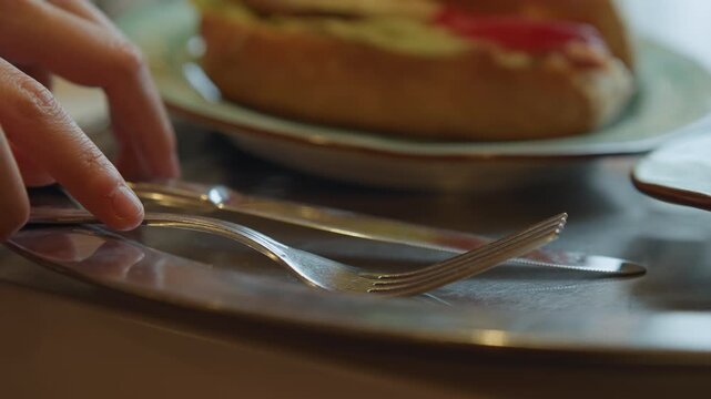 Close up of hand placing silverware on plates with food focusing on action and details. scene includes blurred background elements like additional dishes or table settings emphasizing