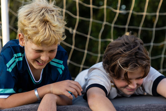 young boys smiling , lying down with soccer net in background at sunset