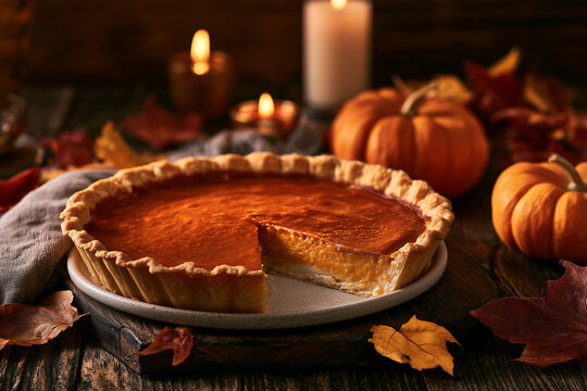 Traditional pumpkin pie with a missing slice on a ceramic plate, surrounded by pumpkins and autumn leaves in warm candlelight
