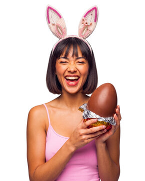 Excited Hispanic woman wearing bunny ears headband holding a large wrapped chocolate Easter egg