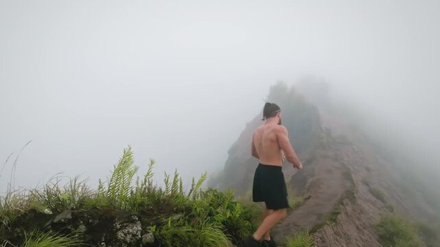 Muscular man flexing his arms, standing shirtless on a misty mountain ridge overlooking the natural landscape of mount Batur in Bali, embodying fitness, strength, and adventure