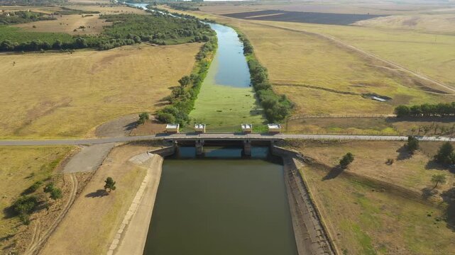 Drone shot of a water control dam and sluice gate on the Tamis River. Concept of agricultural irrigation infrastructure, river flow management, and civil engineering. 4K aerial view.
