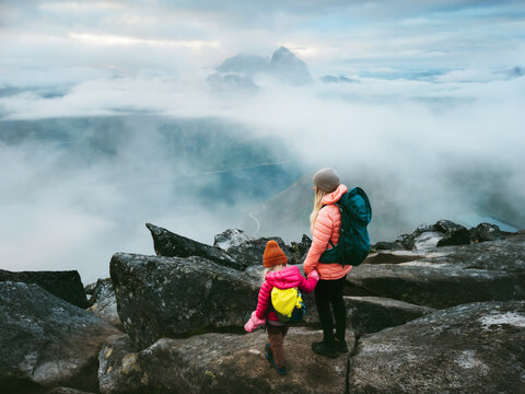 Parent and child hiking together in Norway climbing foggy Segla mountain summit, family travel backpacking outdoor adventure lifestyle active vacations mother and kid trekking explore Senja together