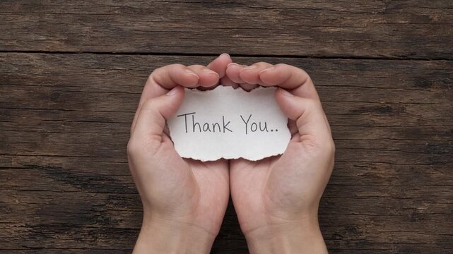 A heartwarming expression of gratitude with hands holding a handmade thank you note on a rustic wooden table surface