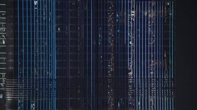 Vertical blue LED light strips pulse and flash across the modern glass facade of a high rise building at night