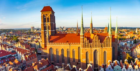Aerial view capturing the historic St. Mary's Church in Gdansk surrounded by colorful rooftops in warm sunlight. The scene highlights the architectural beauty and cultural richness of the city © Kotangens
