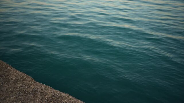 Calm blue sea water gently ripples against a weathered concrete pier edge, capturing a peaceful waterfront mood, 4K.