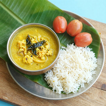 Traditional south indian meal fish curry with rice and tomatoes on banana leaf