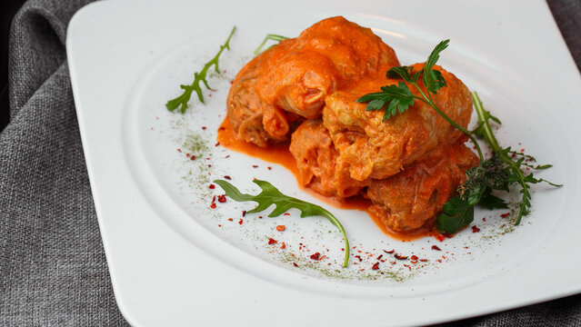 Stuffed Cabbage Rolls in Tomato Sauce with Fresh Herbs on White Restaurant Plate