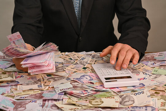 Hands organizing Ukrainian currency with calculator among banknotes, cash management concept showing financial control, payment evaluation, commercial accounting and economic planning in business
