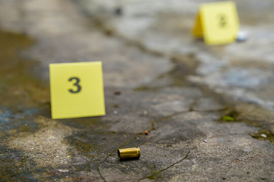 Spent bullet casing lying on concrete floor at a crime scene marked with yellow forensic evidence markers for investigation.