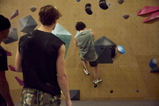 Young men bouldering together on an indoor climbing wall, training and spotting at a climbing gym