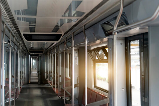 Interior view of a modern commuter train carriage showing rows of empty red seats and sunlight shining through windows during the quiet morning hours